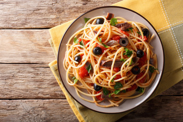 Traditional pasta alla puttanesca with anchovies, tomatoes, garlic and black olives close-up on a...