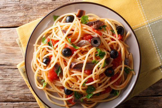 Spaghetti alla putanesca with anchovies, tomatoes, garlic and black olives close-up. horizontal top view
