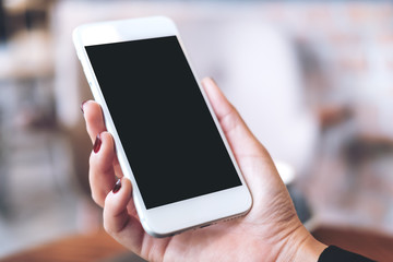 Mockup image of a hand holding white mobile phone with blank black desktop screen with blur background