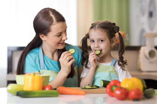 Cute child tasting vegetables as she prepares a meal with their mother in the kitchen