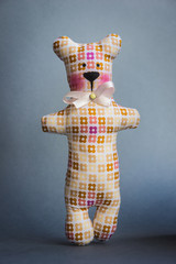 A soft reddish-brown toy bear with a bow-knot and a brooch stands stretching out its paws.