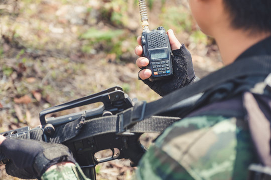 Closeup image of an armed soldier holding and using radio communication in the battle field