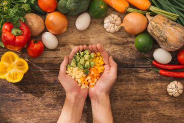 Chopped vegetables on chef hands and ingredients for tasty vegetarian cooking. Top view.