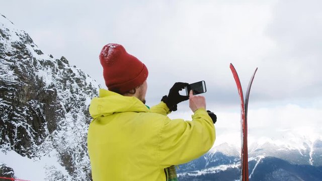 The skier takes photos of the skis on the smartphone and a beautiful mountain view, 4k.