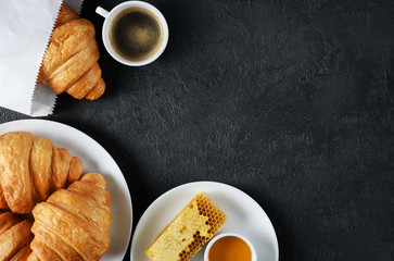 Croissants, coffee and honey on a dark background. Breakfast flat lay.