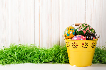Easter eggs in bucket on white wooden background with green grass