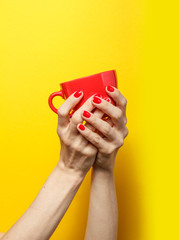 Hand holding the red mug on a bright yellow background