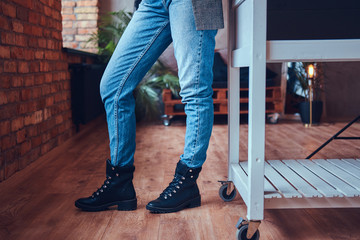 Close up of girl legs in jeans and boots on the wooden floor.