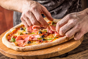 Pizza and Chef. Chef in the restaurant prepares a pizza and decorates it with  prosciutto