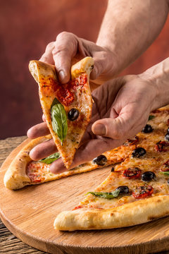 Pizza. Tasty fresh italian pizza served on old wooden table. A piece of pizza in a mans hand