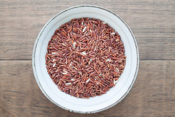 Fototapeta na wymiar Top view of raw brown rice in ceramic bowl on wooden table, Healthy food