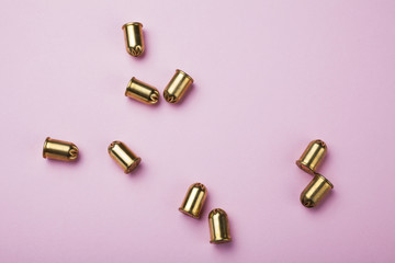 Spilled golden blank cartridges and bullets on a pink background.