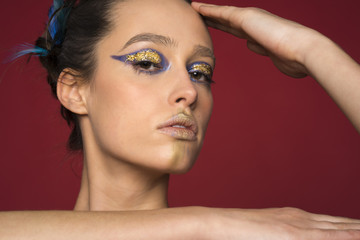 Portrait of a beautiful young girl with a chignon decorated with feathers and a gold and blue makeup