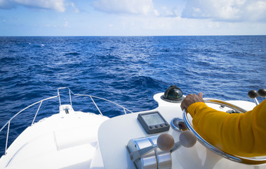 Hand of captain on steering wheel of motor boat in the blue ocean due the fishery day