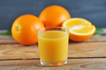 glass with fresh orange juice on the background of whole oranges