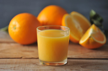 glass with fresh orange juice on the background of whole oranges