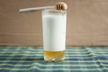 a glass of milk with honey  and wooden spoon on tablecloths