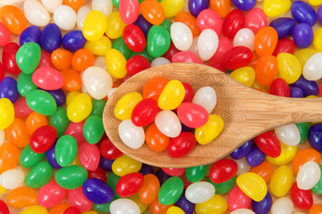 Fototapeta na wymiar Many brightly colored jelly beans in a rainbow of colors. Popular candy for Easter. wooden spoon on top of pile with variety of colored candy inside