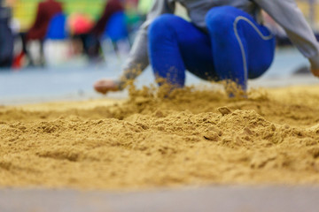 Fototapeta na wymiar Sportsman landing into sandpit on training in long jump. Track and field competitions concept background