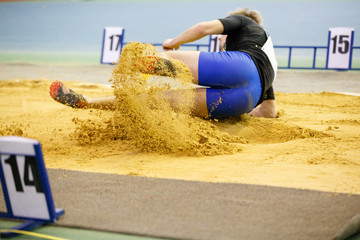 Sportsman landing into sandpit in long jump competition. Track and field competitions concept background