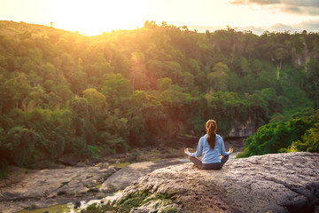 Yoga woman sit in lotus pose on mountain peak rock at sunrise