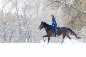 Young rider girl on bay horse galloping in winter. Equestrian winter activity background