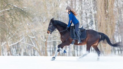 Young rider girl on bay horse galloping in winter. Equestrian winter activity background