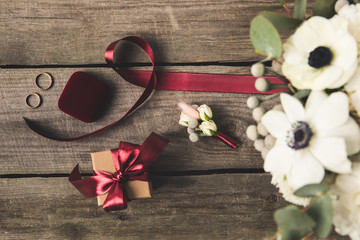 flat lay with ribbon, wedding rings, corsage and gift on wooden tabletop