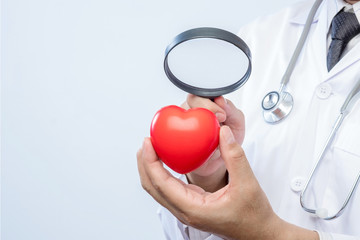 Professional medical doctor holding a magnifying glass check up on a red heart ball. Concept of...