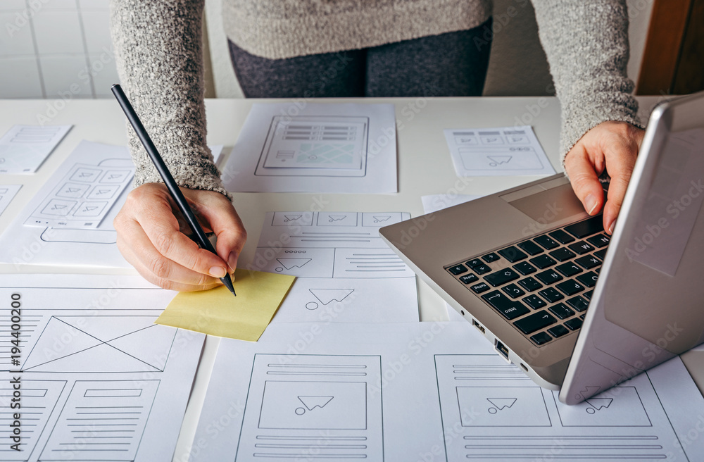 Wall mural web designer working at laptop and website wireframe sketches on white table