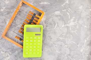 Old scratched wooden brown abacus and new green plastic solar calculator on gray broken cement. Top...