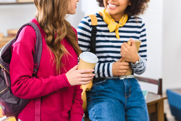 partial view of multiethnic students with coffee to go and book