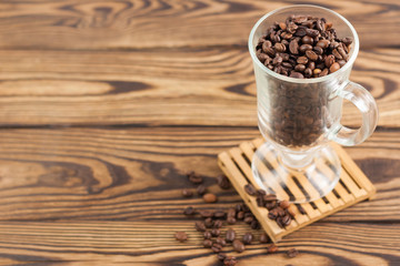 Lot of fried coffee beans in transparent glass for mulled wine on pallet and scattered coffee beans on old wooden rustic brown table