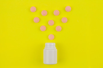 Double color whole pills poured out of plastic container in form of heart on background of yellow paper. Top view