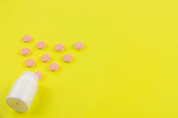 Double color whole pills poured out of plastic container in form of heart on background of yellow paper