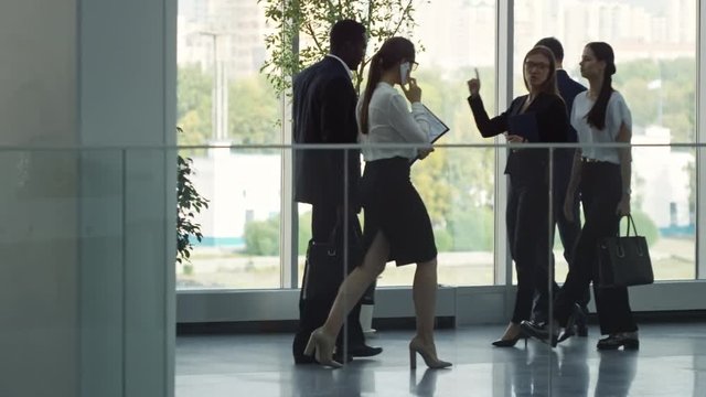 PAN with slowmo of busy people in formal work attire walking through lobby of business centre