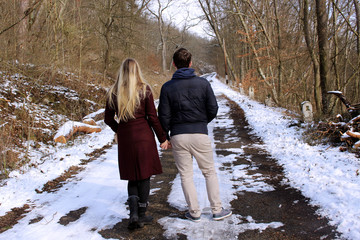 A beautiful couple walking on a snowy road in the woods .People, season and leisure.