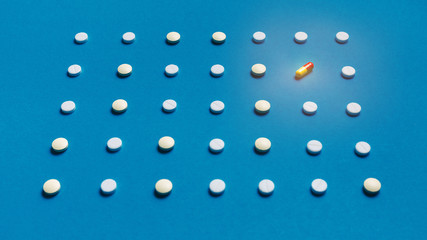 Pattern With Rows White Tablets And One Colored Pill On Blue Background, Top View. Medicine Pharmacy Concept