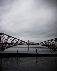 Two people walking along a pier infant of the Forth bridges - 194404049