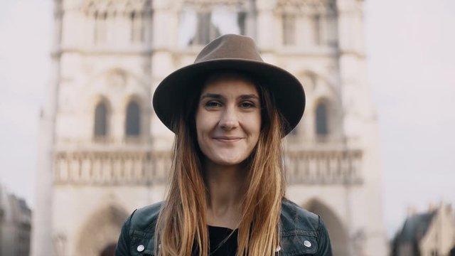 Portrait of young beautiful woman in hat near the Notre Dame in Paris, France. Female looking at camera and smiling.