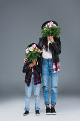 mother and daughter covering faces with bouquets on grey