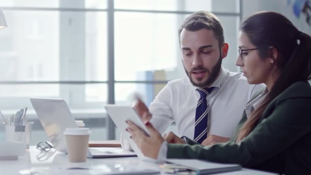 Businessman and businesswoman working together at desk in the office: they discussing something on tablet screen and analyzing financial documents