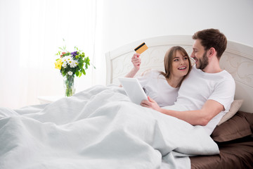 Obraz na płótnie Canvas Couple doing online shopping while lying in cozy modern bedroom