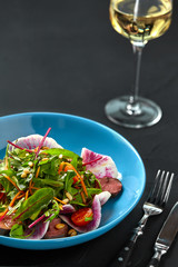 Spicy beef slices meat salad with tomatoes, parsley, radish and salad leaves spinach on black texture background table