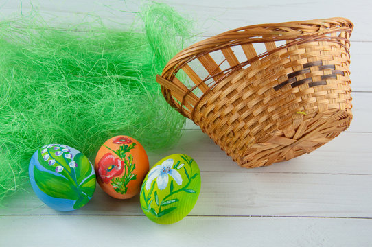 Easter. Drawings on eggs and basket on white wooden background near green sinthetic grass