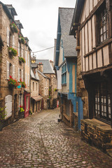 Traditional half-timbered and stone houses decorated with flowers on medieval pedestrian cobbled road in old town of Dinan, Brittany, France