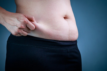 Fototapeta premium Close up female checking fat on abdomen, dark blue background.