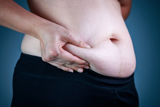 Close up female checking fat on abdomen, dark blue background.