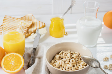 Delicious Healthy breakfast.  Whole Grain Cereal rings, milk, honey and orange juice on the white table. Cheerios whole grain cereals with milk. Healthy lifestyle.