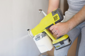 The man with a beard paints white walls with the paint spray. Repair in the house